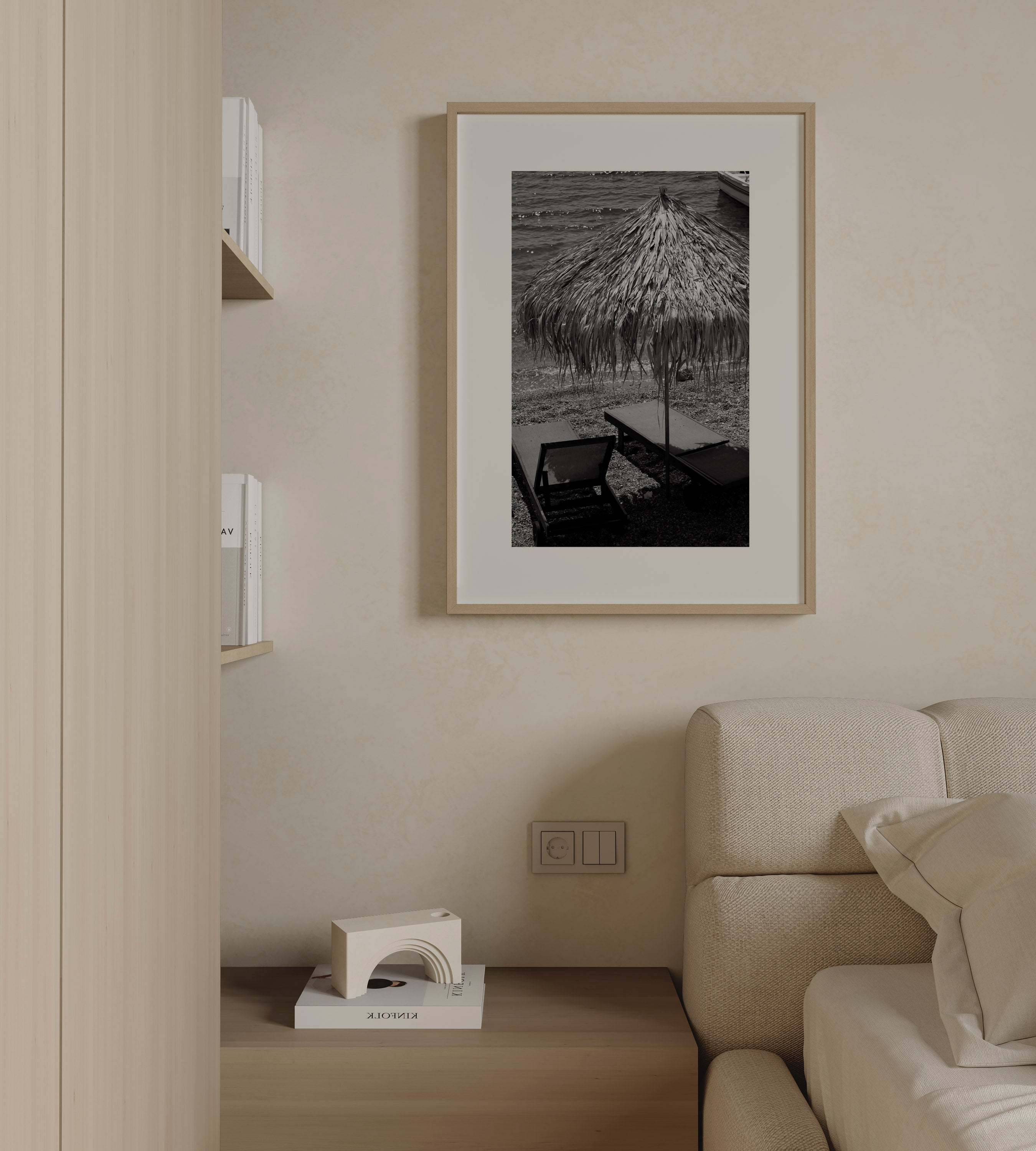 Seaside Pause by Daniel Barlot – black and white Fine Art photograph of a quiet Mediterranean beach with a traditional straw umbrella and empty sun loungers, captured in Greece and framed in natural oak.