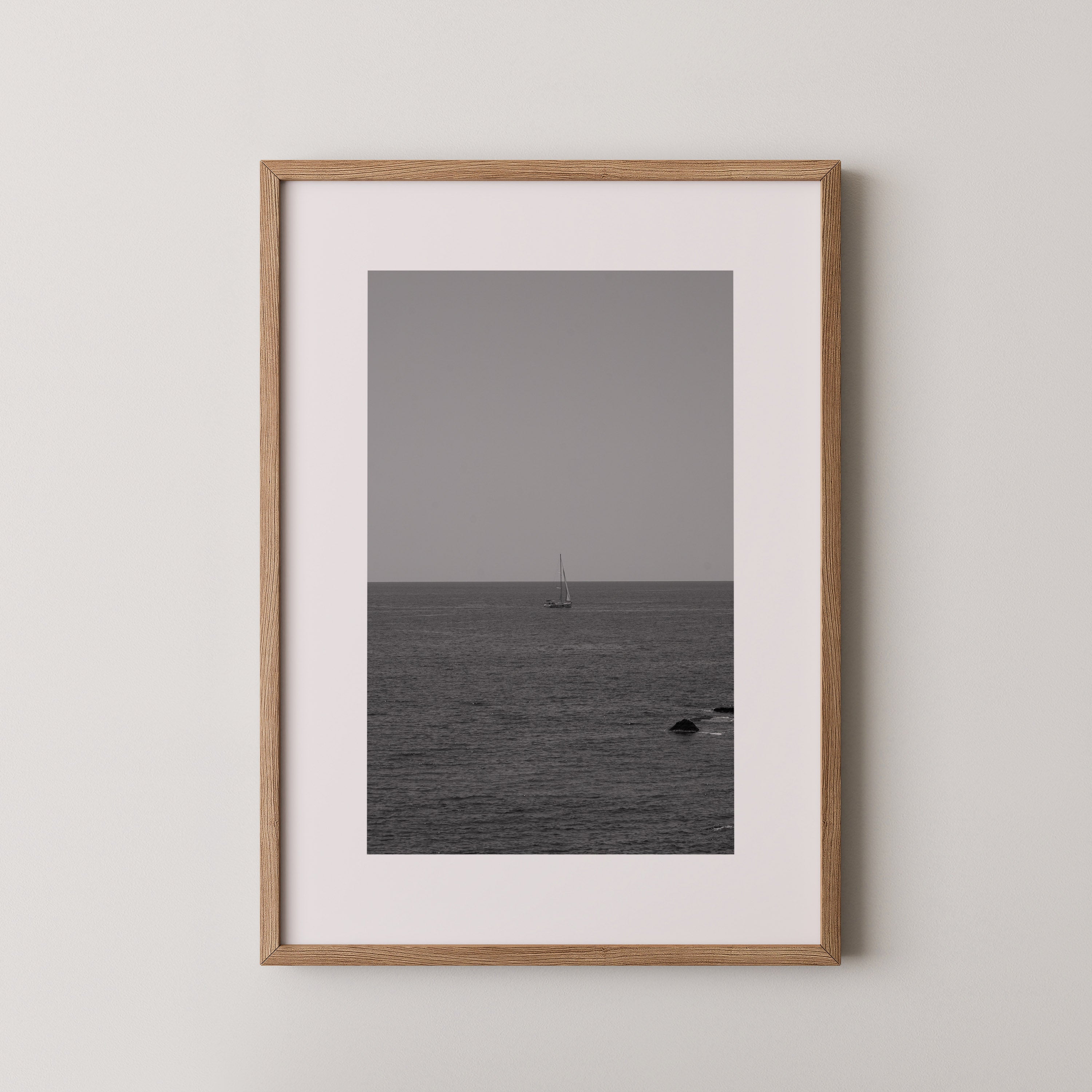 The Quiet Voyage by Daniel Barlot – minimalist black and white fine art photograph of a lone sailboat sailing across the Mediterranean horizon, framed in natural oak.