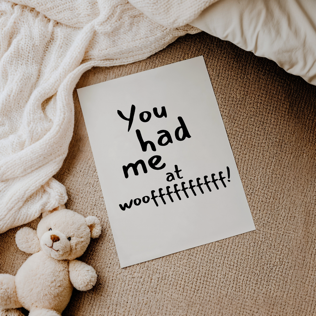 פוסטר טיפוגרפי עם הכיתוב "You had me at woof" בעיצוב שחור מינימליסטי, מונח על שטיח ליד בובת דובי.