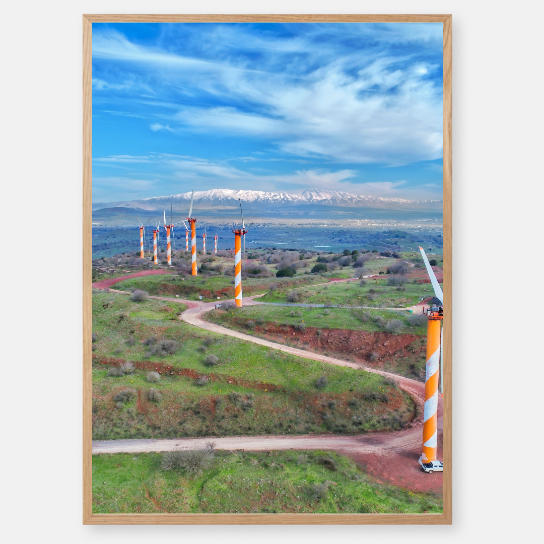 צילום נוף של טורבינות רוח בכתום ולבן באלוני הבשן, ישראל, עם החרמון המושלג ברקע, מאת חן כליפה לוי.