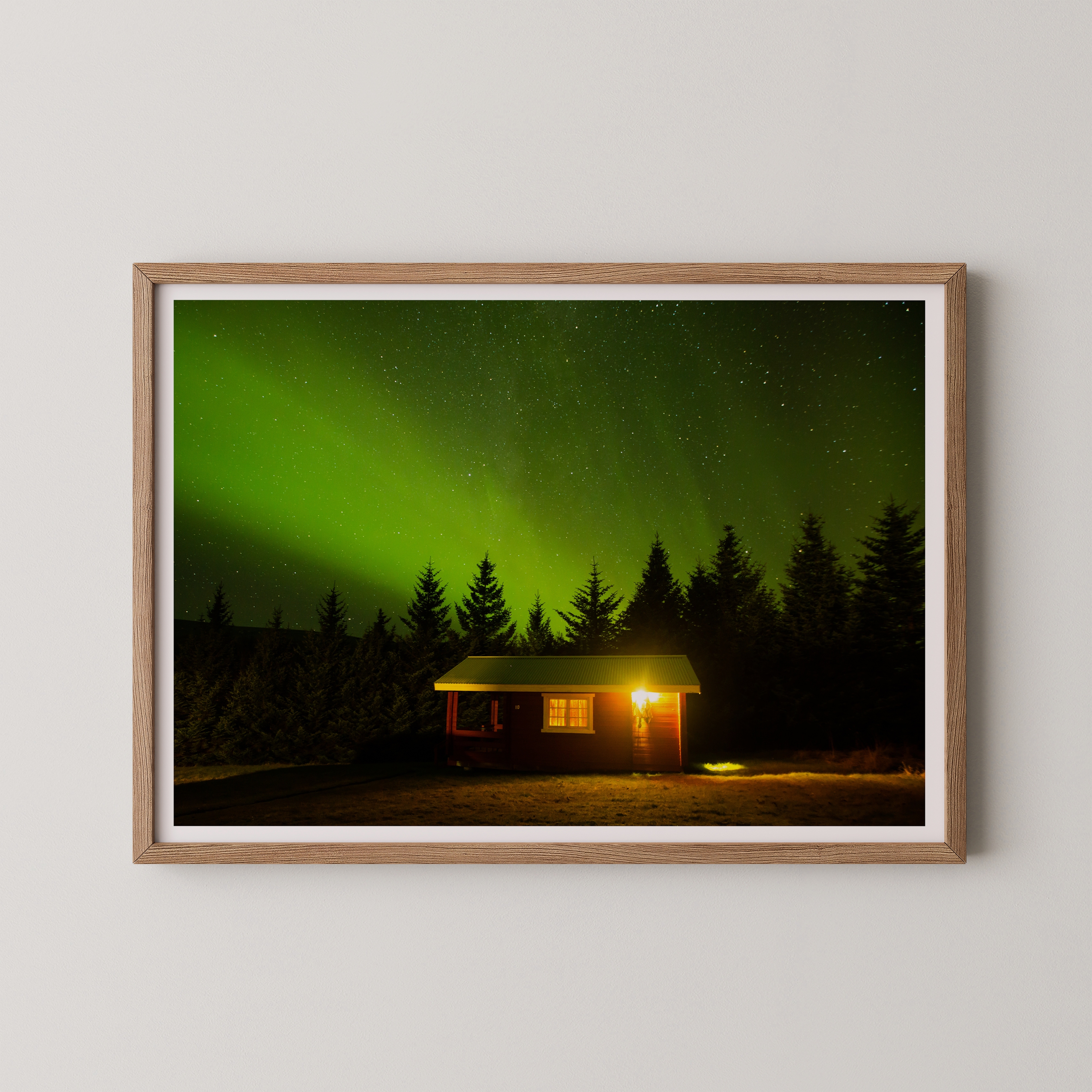 צילום אומנותי של בקתה מוארת בלב היער תחת מופע הזוהר הצפוני באיסלנד, מאת הצלם דניאל עובדיה.