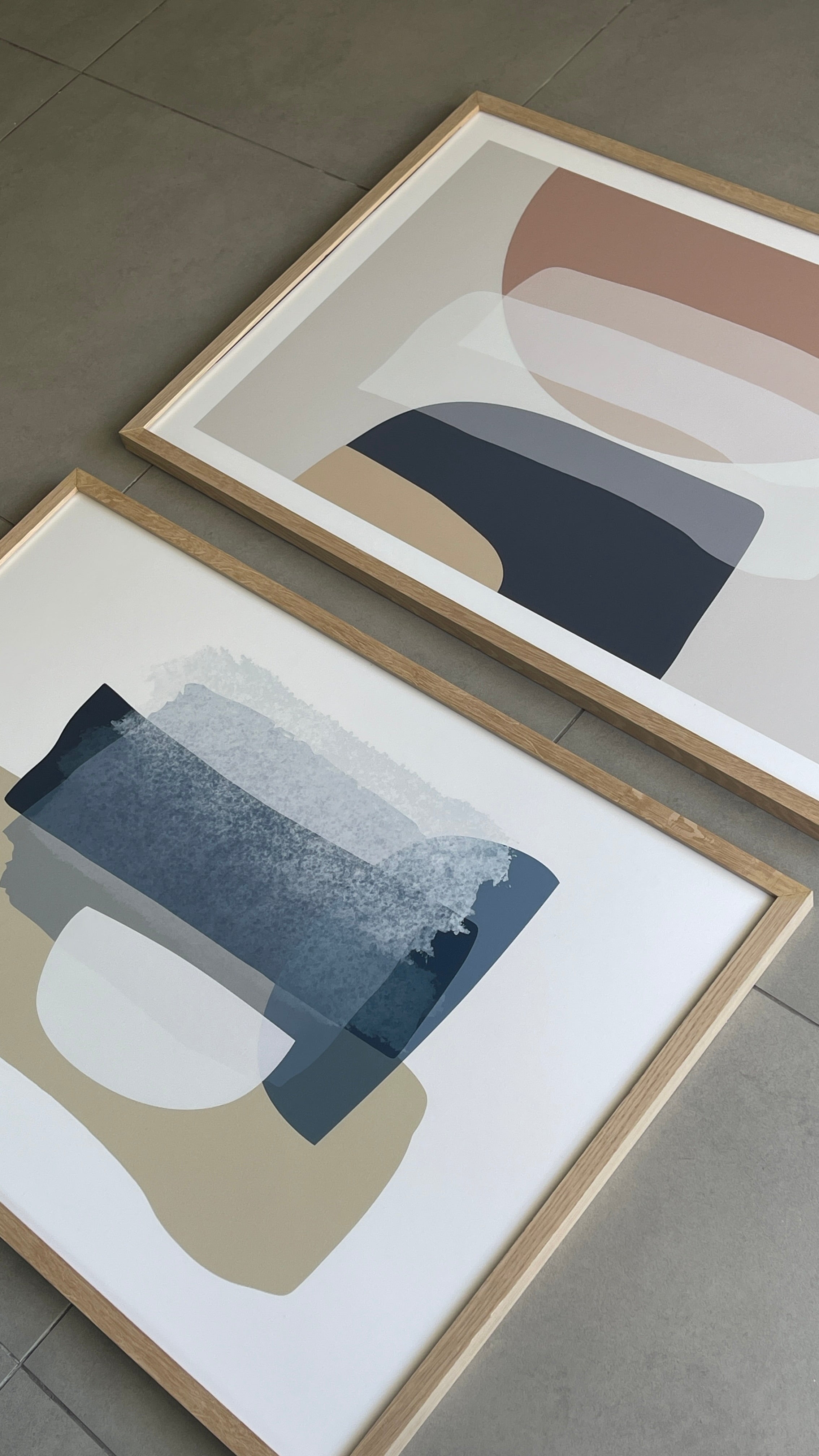 סט של שני פוסטרים ממוסגרים בסגנון אבסטרקטי, עם צורות אורגניות בגווני בז', כחול עמוק ואפרסק, המשדרים הרמוניה ורוגע.