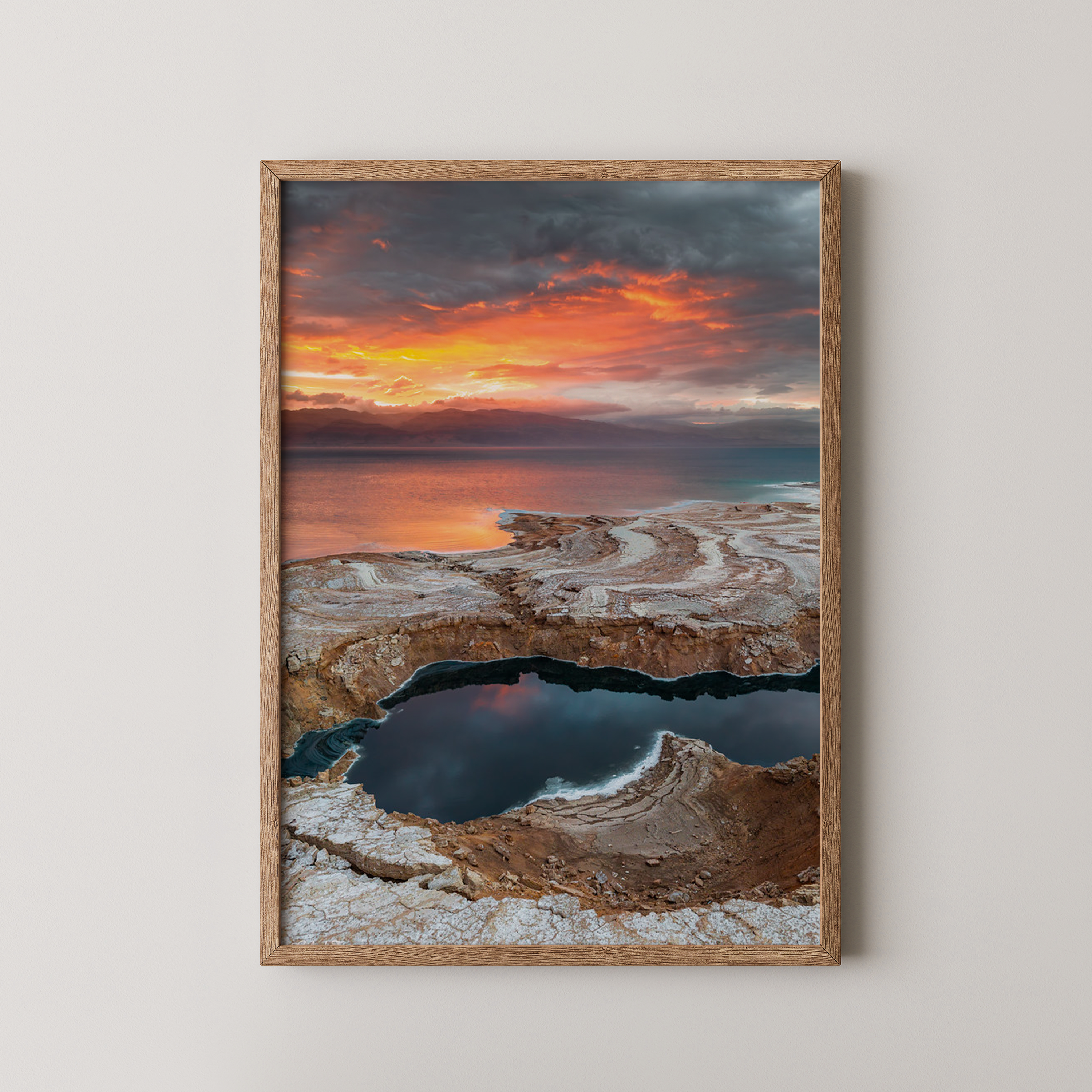 יצירה ממוסגרת של גלעד טופז בצילום זריחה בעין גדי, שמיים כתומים דרמטיים משתקפים בבריכות מים ומלח לאורך חוף ים המלח
