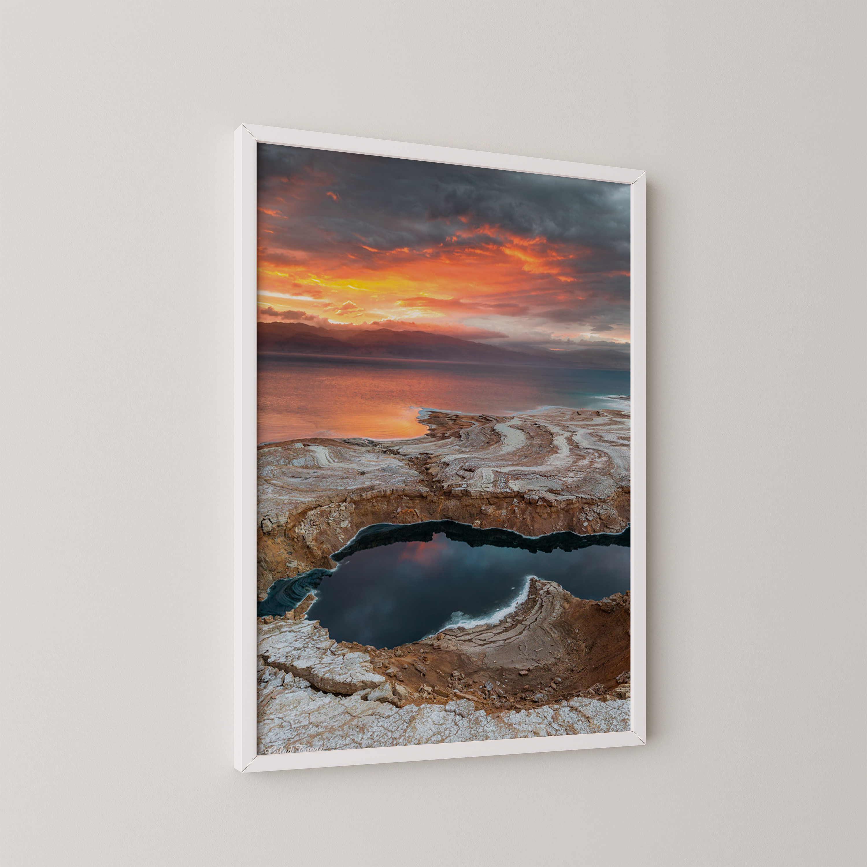 יצירה ממוסגרת של גלעד טופז בצילום זריחה בעין גדי, שמיים כתומים דרמטיים משתקפים בבריכות מים ומלח לאורך חוף ים המלח