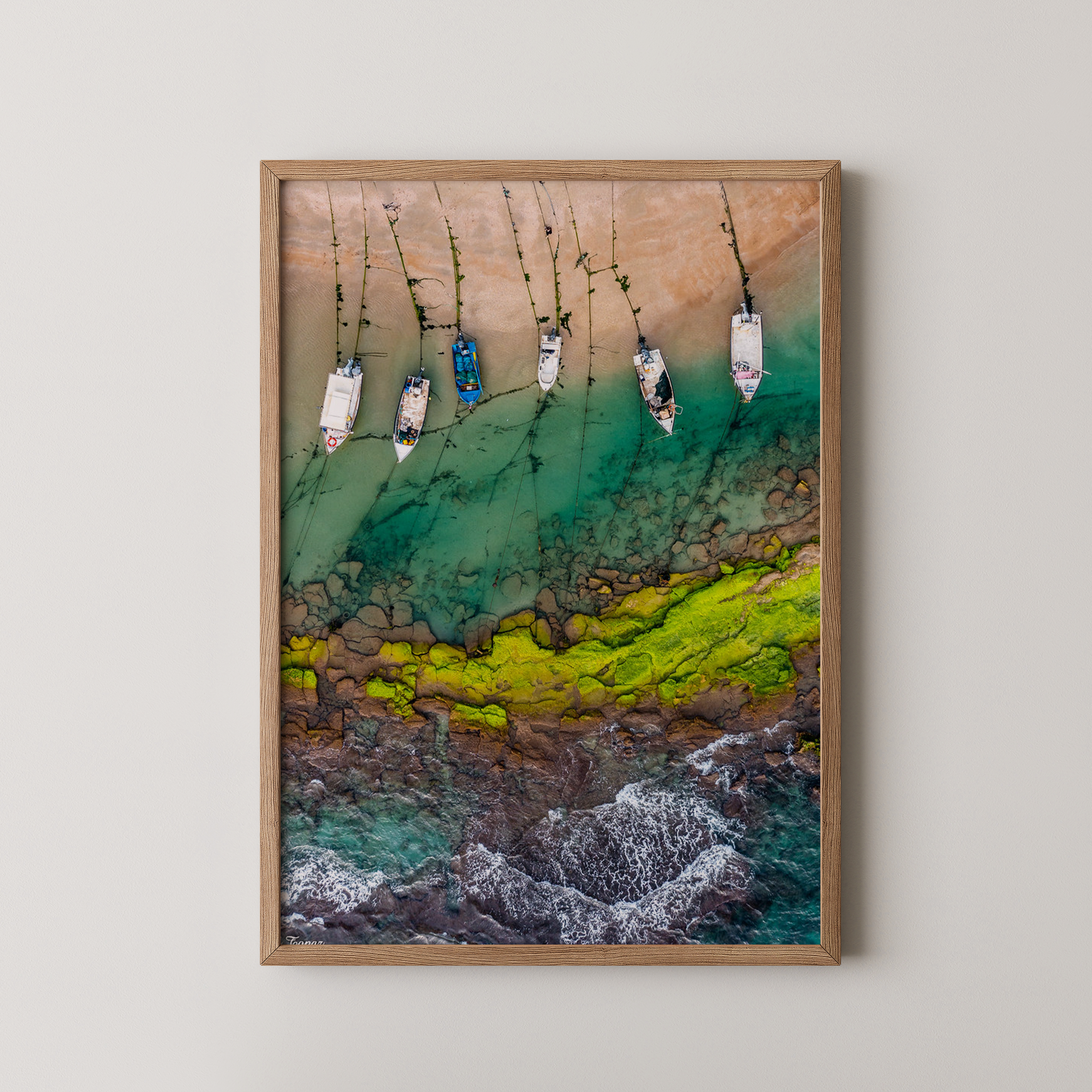 יצירה ממוסגרת של גלעד טופז בצילום אווירי של סירות דייגים עוגנות במים רדודים וטורקיז לאורך חוף סלעי בחדרה