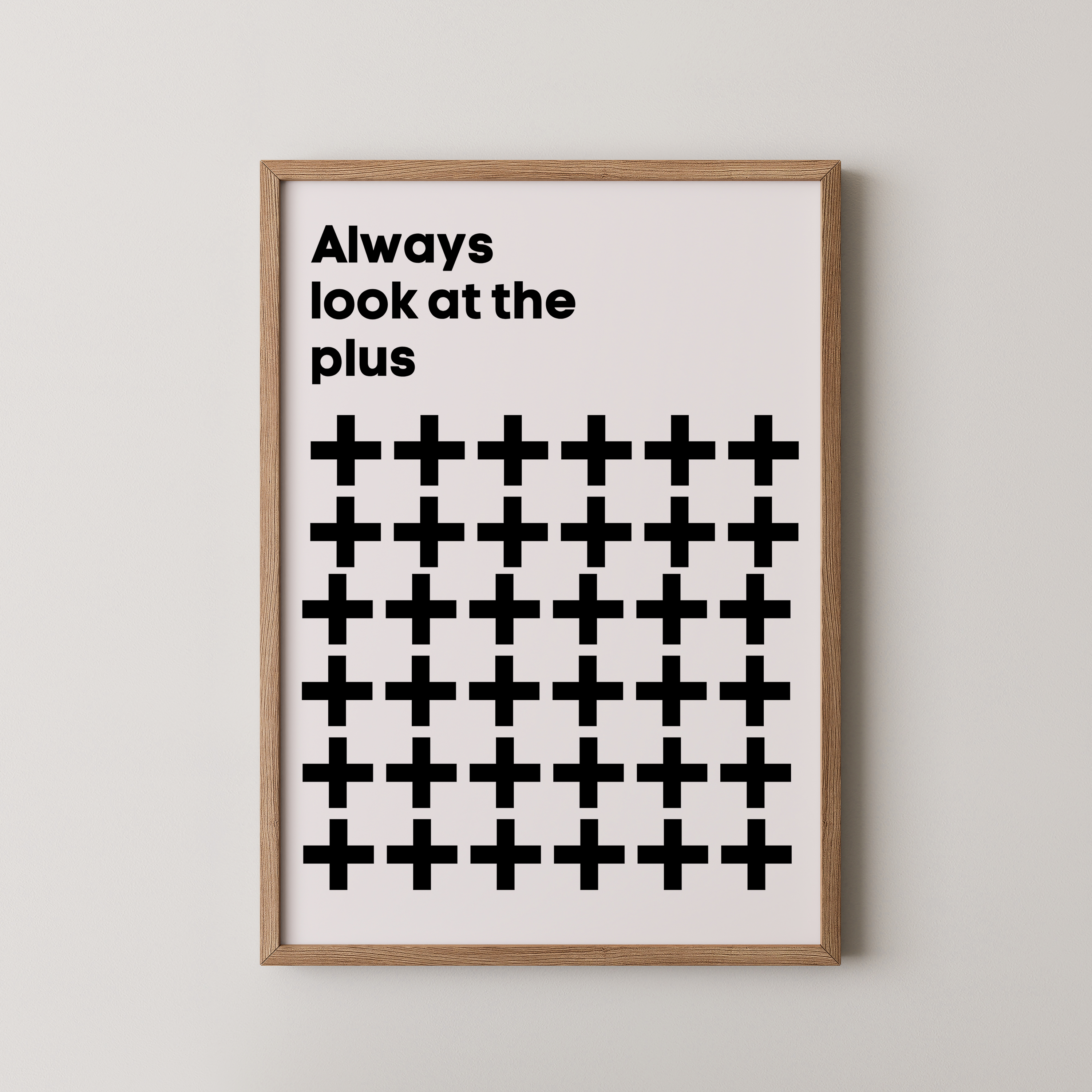 יצירת קיר טיפוגרפית Always Look at the Plus עם גריד של סימני פלוס שחורים במסגרת עץ טבעי, בסגנון מודרני ומינימליסטי.