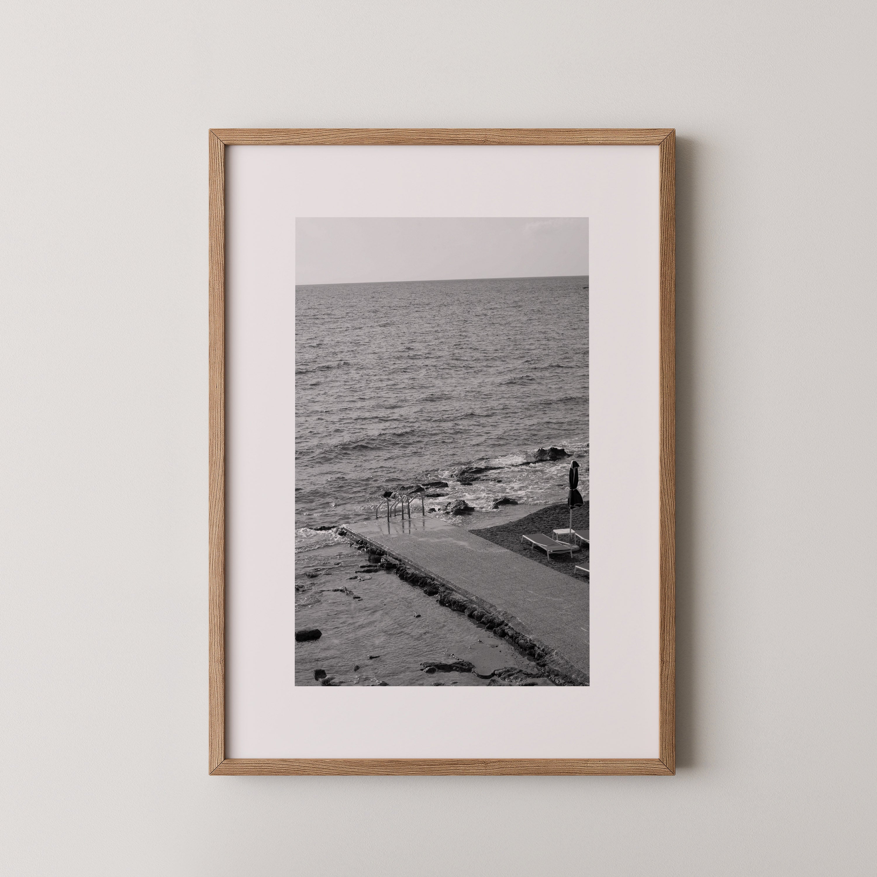 The Quiet Pier by Danielle Berlot – צילום אמנותי בשחור־לבן של מזח שקט היוצא אל הים ברודוס, במסגרת עץ אלון.