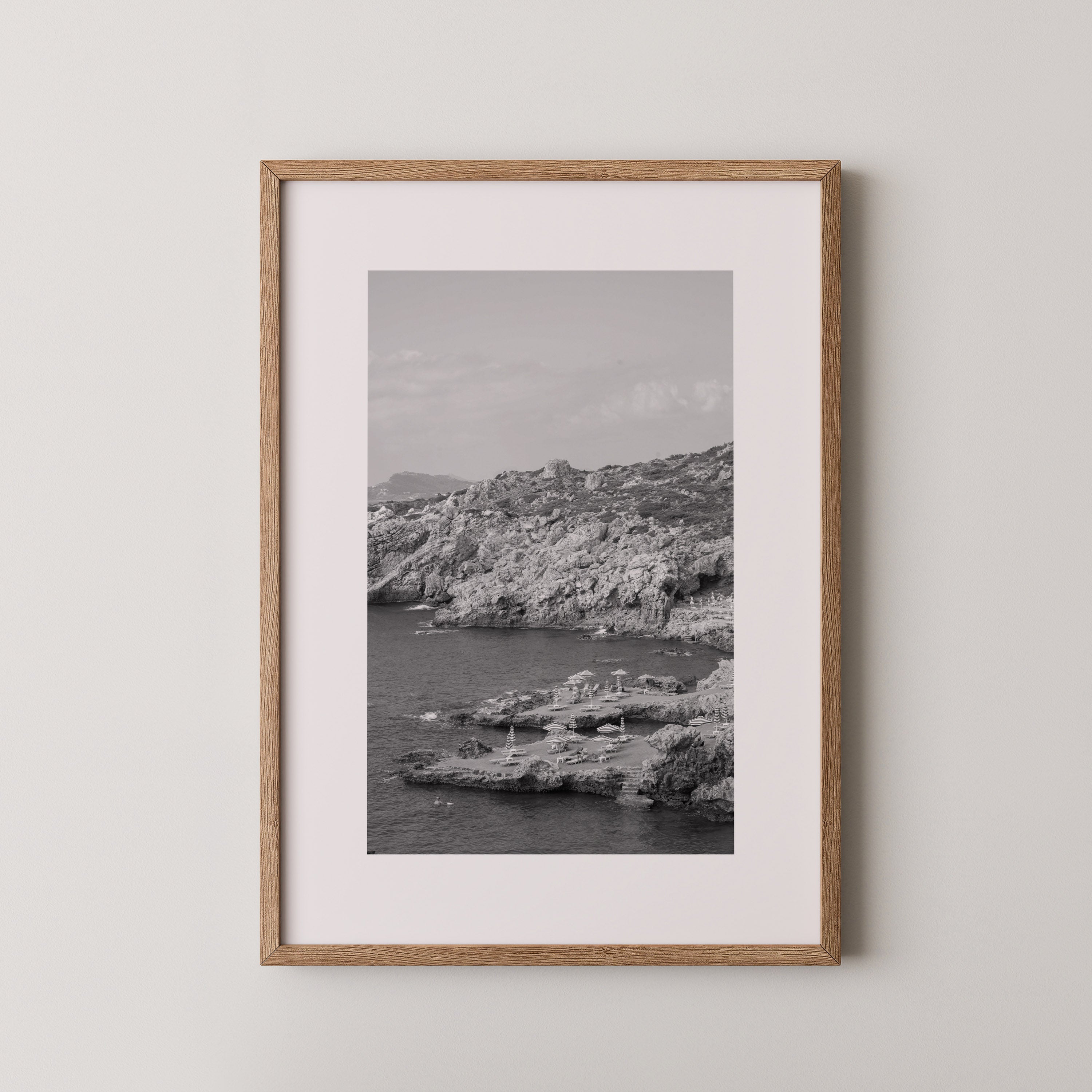 Shoreline Calm by Daniel Barlot – black and white fine art photograph of a tranquil Mediterranean rocky shoreline captured in Greece, framed in natural oak.