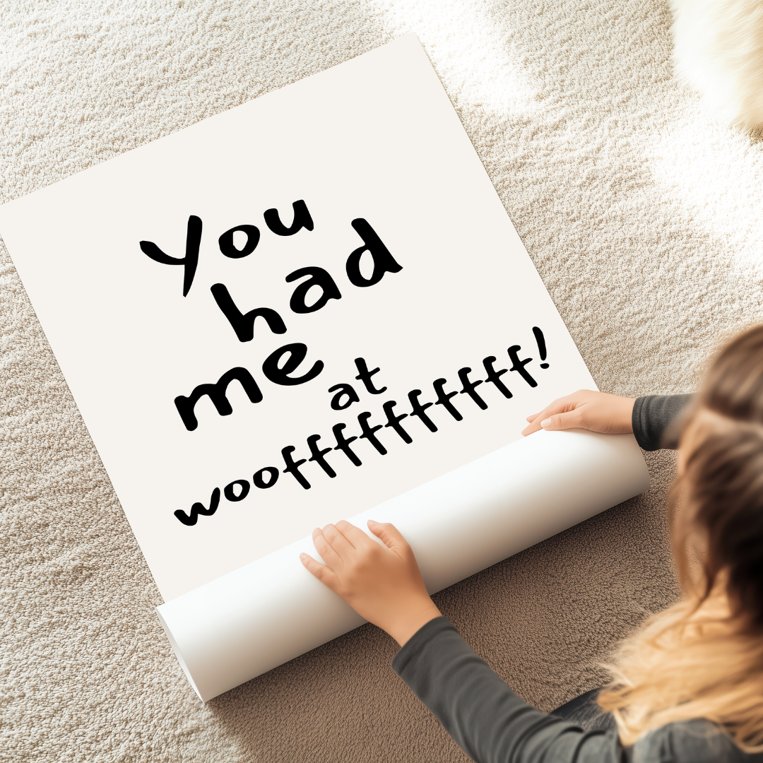 פוסטר טיפוגרפי עם הכיתוב "You had me at woof" בעיצוב שחור מינימליסטי, מונח על שטיח ליד בובת דובי.

