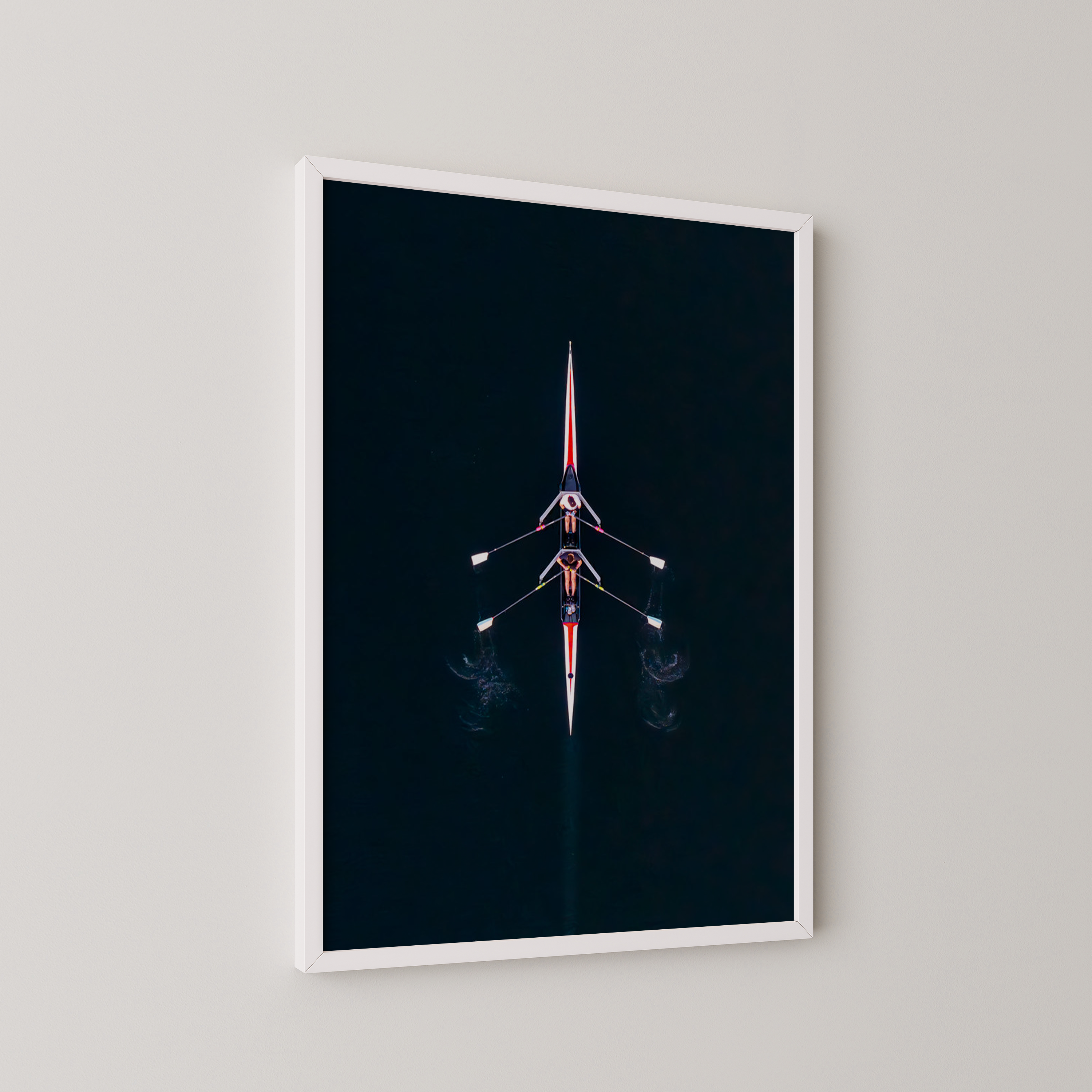 יצירה ממוסגרת של גלעד טופז בצילום אווירי של סירת חתירה במרכז נהר הירקון, מים כהים וסימטריה מינימליסטית מעל קיר בהיר