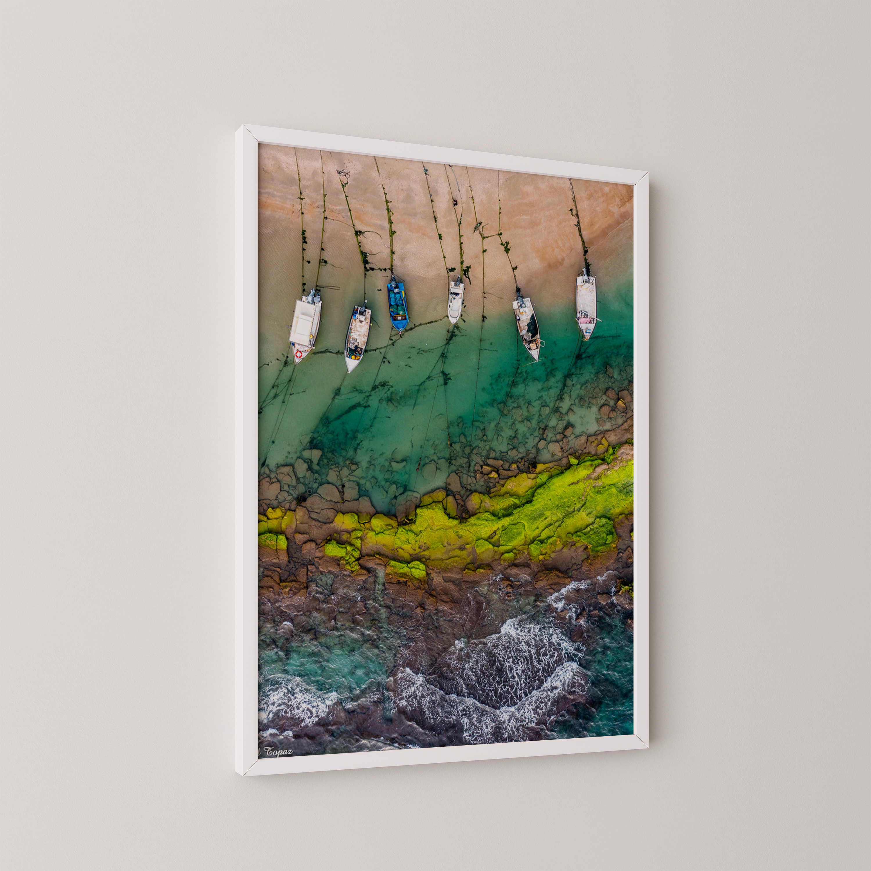 יצירה ממוסגרת של גלעד טופז בצילום אווירי של סירות דייגים עוגנות במים רדודים וטורקיז לאורך חוף סלעי בחדרה