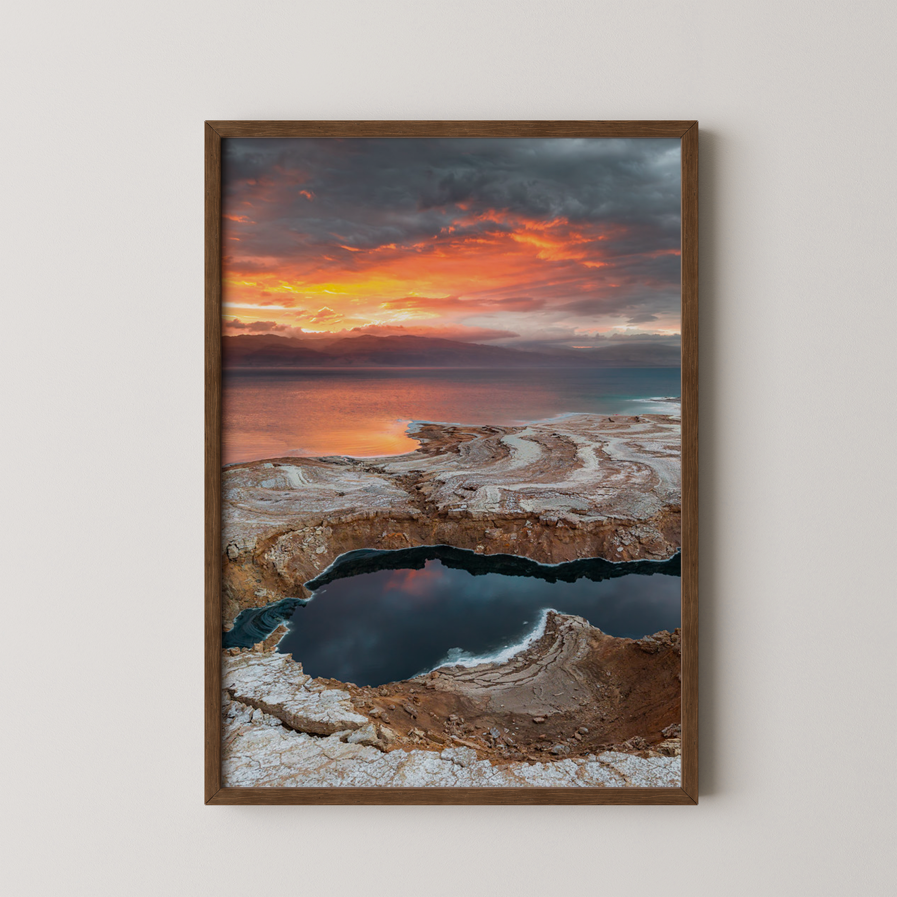 יצירה ממוסגרת של גלעד טופז בצילום זריחה בעין גדי, שמיים כתומים דרמטיים משתקפים בבריכות מים ומלח לאורך חוף ים המלח