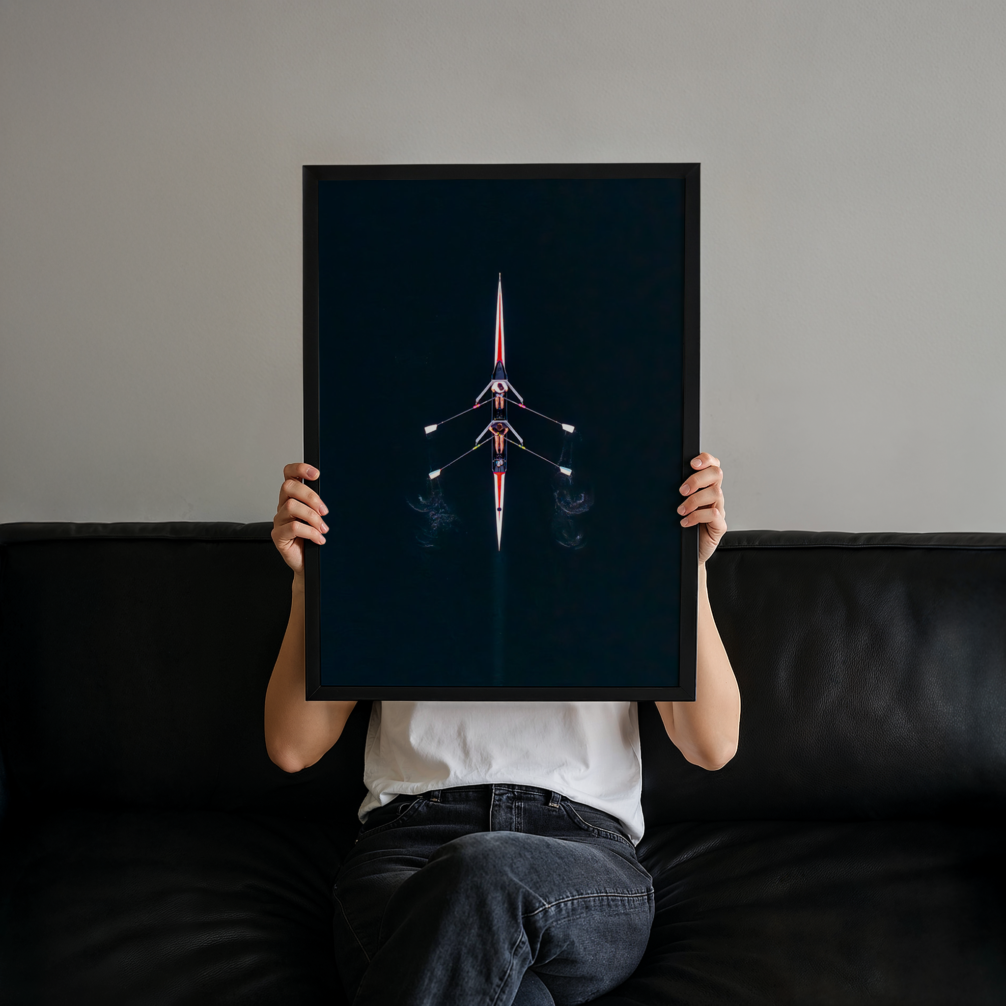 יצירה ממוסגרת של גלעד טופז בצילום אווירי של סירת חתירה במרכז נהר הירקון, מים כהים וסימטריה מינימליסטית מעל קיר בהיר